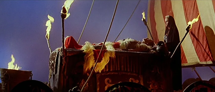 Erik The Conqueror (1961) movie still: wide — A dark night setting features an elevated platform surrounded by burning torches. A woman stands over…