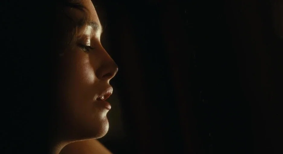 Atonement (2007) movie still: closeup — A dark environment surrounds a person positioned in a side profile view. The person appears to have eyes…