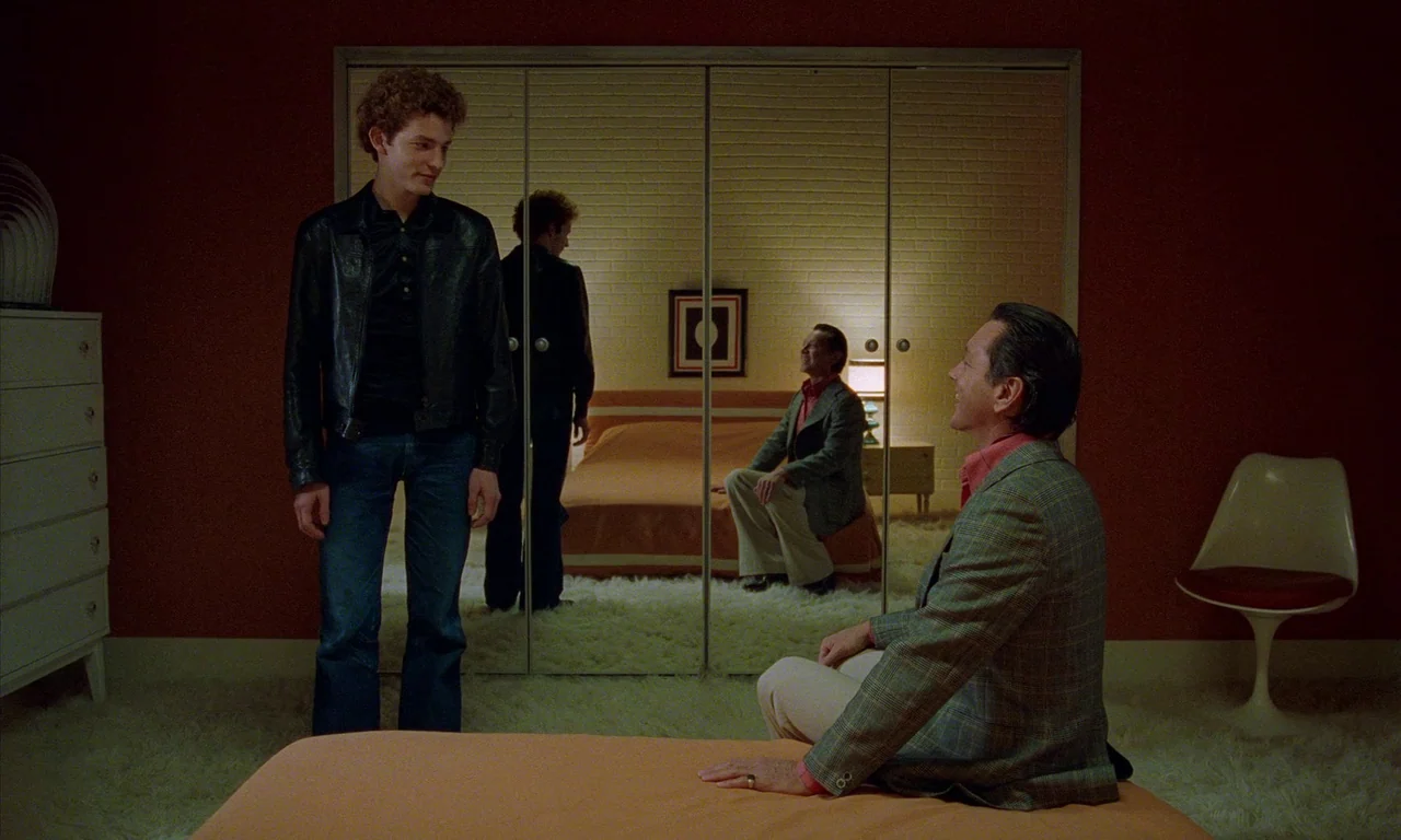 Water Drops on Burning Rocks (2000) movie still: wide — A 1970s bedroom features red walls, white shag carpeting, and large mirrored wardrobe doors.…