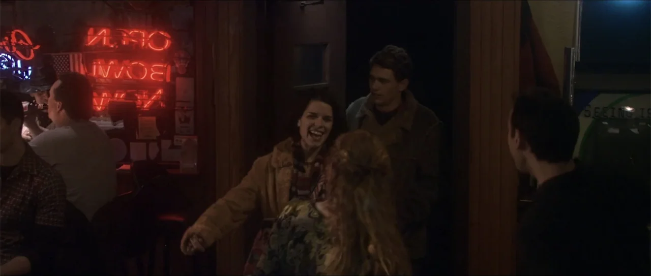El acto (1989) movie still: medium — A dark tavern interior features a bright red neon sign in the window. Two young adults stand together in a…
