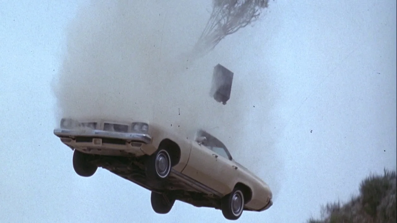 Army of Darkness (1992) movie still: wide — A light-colored sedan floats in mid-air over a sloped hillside during a crash. Dust and debris particles…