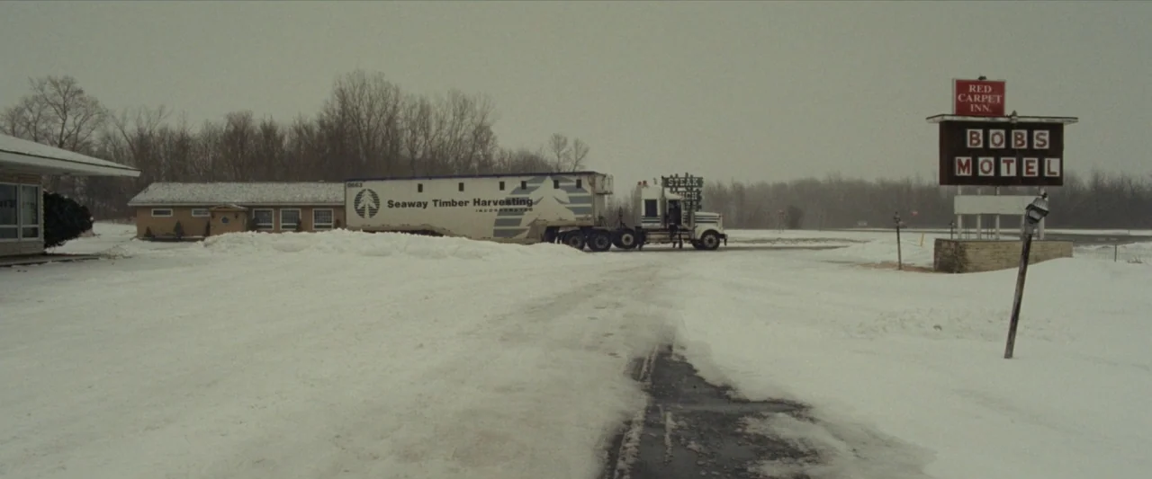 For Ellen (2012) movie still: wide — A snow-covered parking lot in front of a motel during a winter day. A semi-truck is parked near the main…