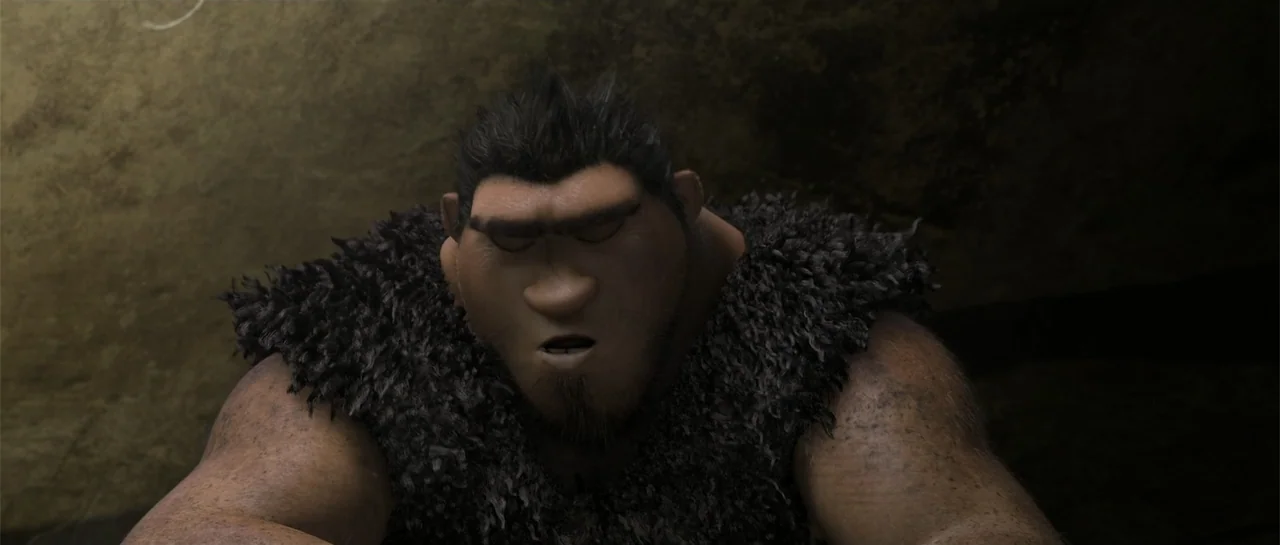 The Croods (2013) movie still: medium — A dark, rocky cave interior is sparsely lit with dim, directional light. A muscular prehistoric man with…
