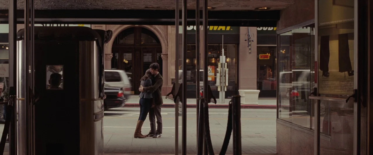 500 Days of Summer (2009) movie still: wide — A city sidewalk visible through the glass entrance of a building lobby. A man and a woman stand on the…