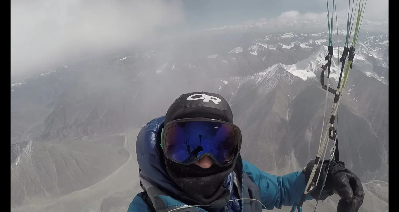 Blutch (2018) movie still: closeup — High altitude view above vast snow-covered mountain ridges under a cloudy sky. A paraglider in heavy winter…