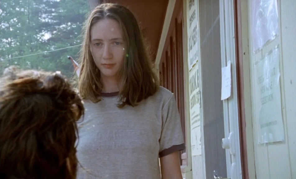 The Brown Bunny (2003) movie still: medium — A woman stands on a wooden porch outside a building with white-painted siding. She looks forward…