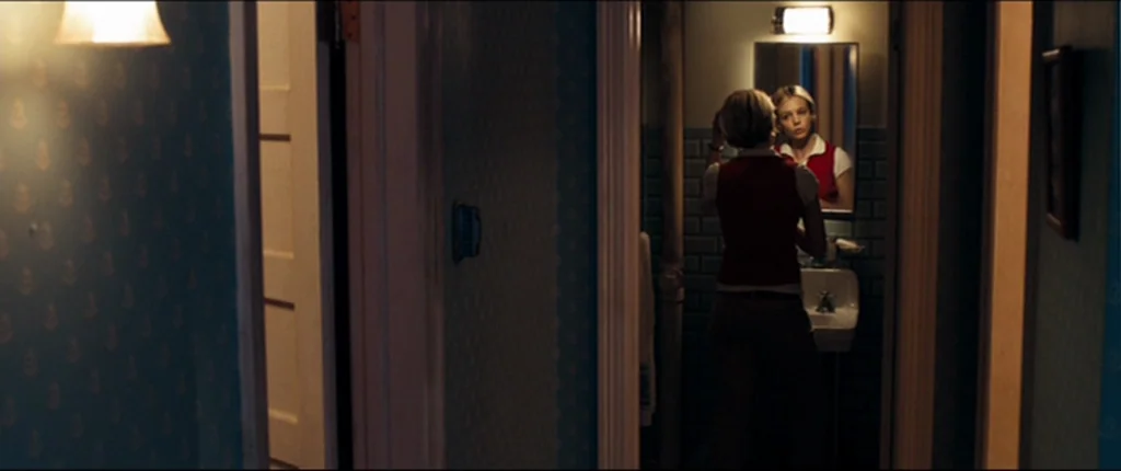 Drive (2011) movie still: medium — A small bathroom with dark tiled walls features a white porcelain sink and mirror. A young woman in a red vest…
