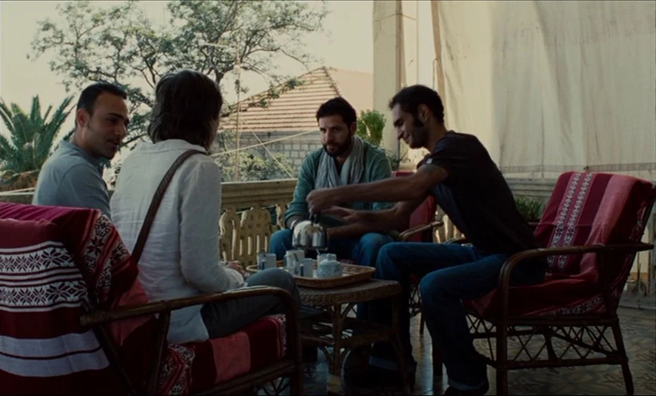 Hadewijch (2009) movie still: medium — A sunny balcony featuring wicker chairs draped with patterned red and white textiles. Four individuals sit…