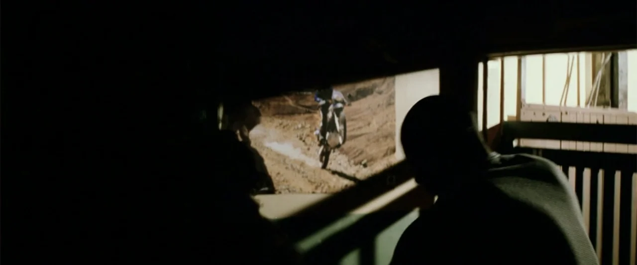 xXx (2002) movie still: medium — A dimly lit room with a television screen displaying a dirt bike on a track. A silhouetted person sits in the…