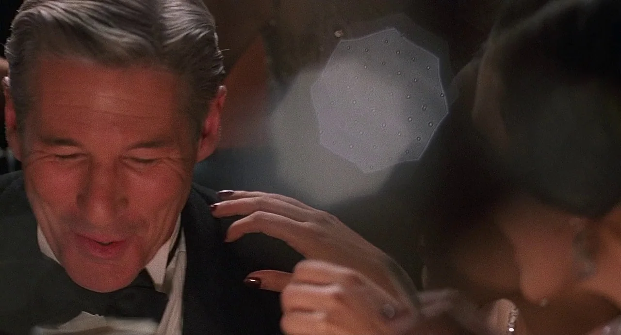 Chicago (2002) movie still: closeup — A dimly lit dinner setting features a man in formal wear. A woman reaches toward his shoulder while dining in…