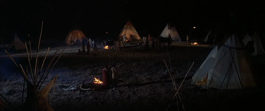 Little Big Man (1970) movie still: wide — A nighttime encampment features several conical dwellings illuminated by small, glowing campfires. People…