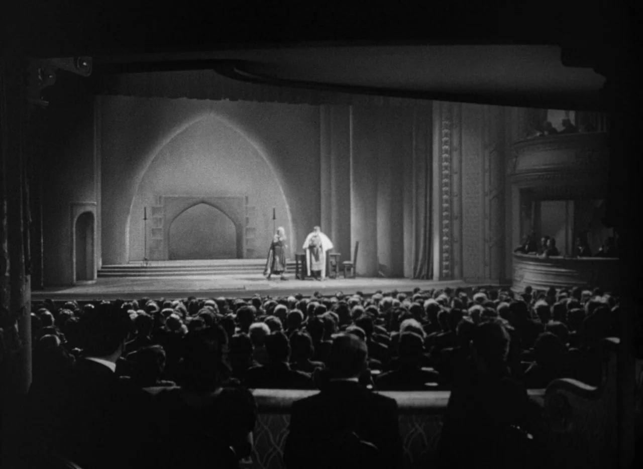 To Be or Not To Be (1942) movie still: wide — An ornate interior of a grand theater with a large audience facing a stage. Two actors perform in…