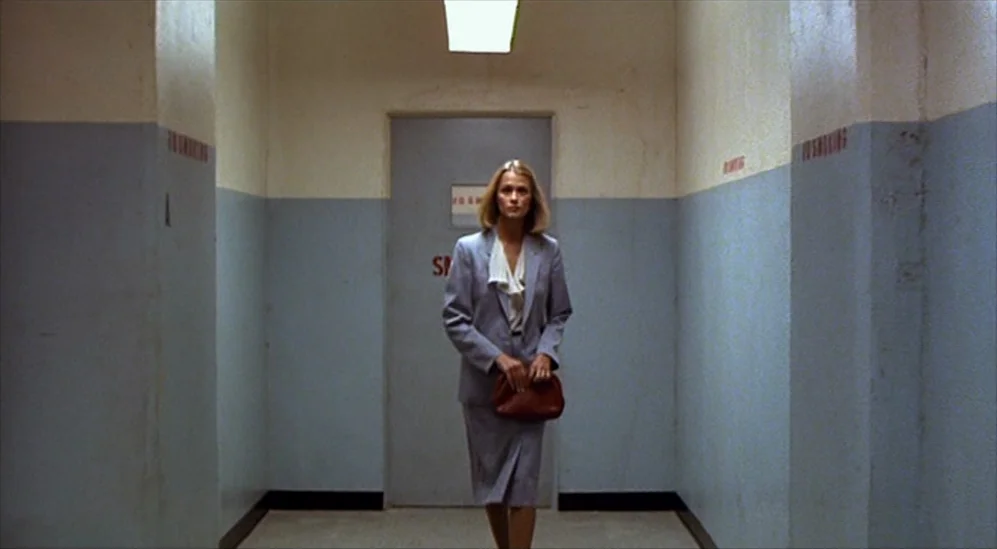 American Gigolo (1980) movie still: fullbody — A narrow industrial-style hallway has light blue paint on the lower half of walls. A woman in a grey…