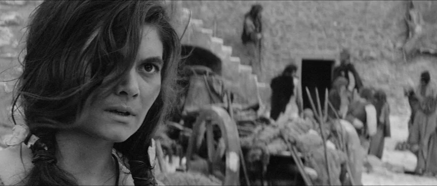 Marketa Lazarová (1967) movie still: closeup — An ancient village settlement features rough stone structures and a wooden horse-drawn cart nearby. A…