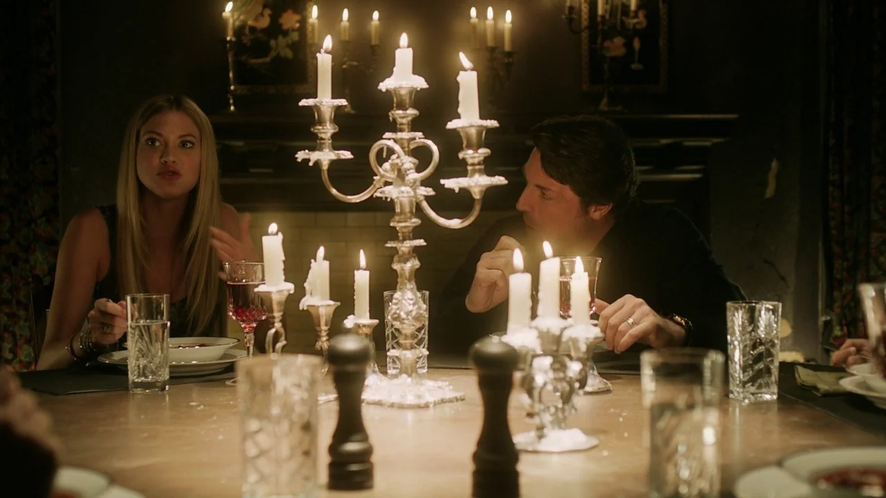 Curse of Chucky (2013) movie still: medium — A dimly lit dining room features a large table set for a formal meal. A man and a woman sit opposite…