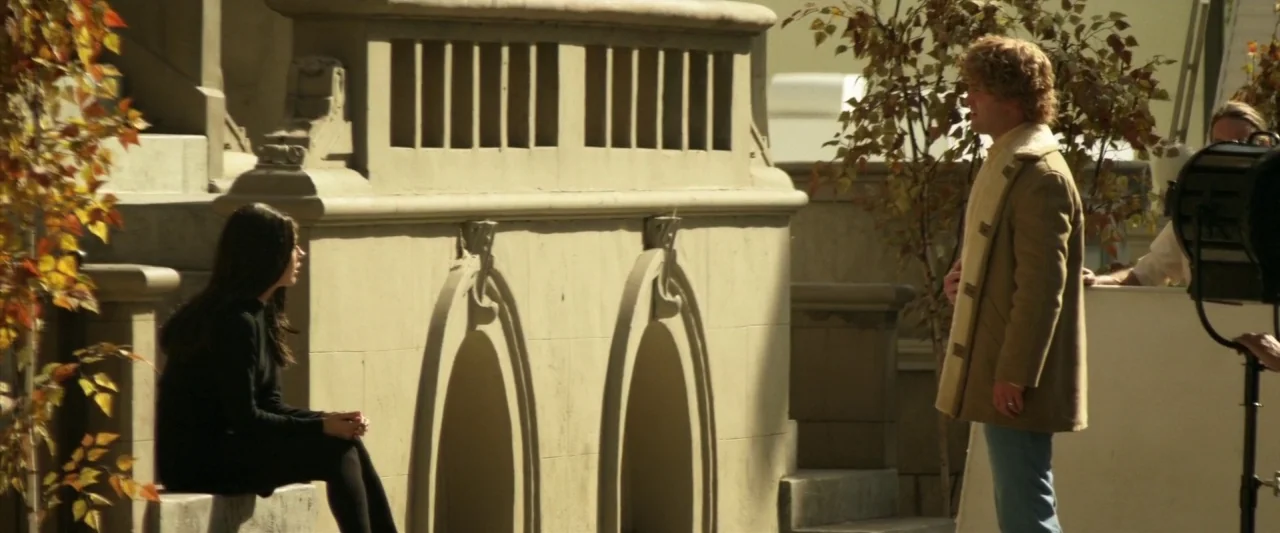 Zeroville (2019) movie still: fullbody — A light-colored stone courtyard features arches and a decorative balustrade with autumn-toned trees. A…