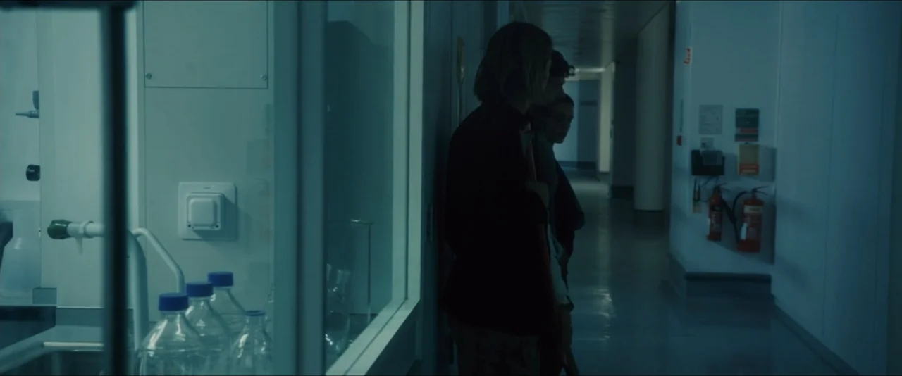 World War Z (2013) movie still: medium — A dimly lit scientific facility corridor features laboratory glass partitions on one side. Two individuals…