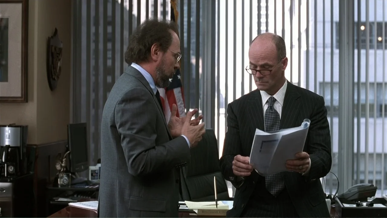 Analyze That (2002) movie still: medium — A high-rise executive office features floor-to-ceiling vertical blinds and an American flag. Two…