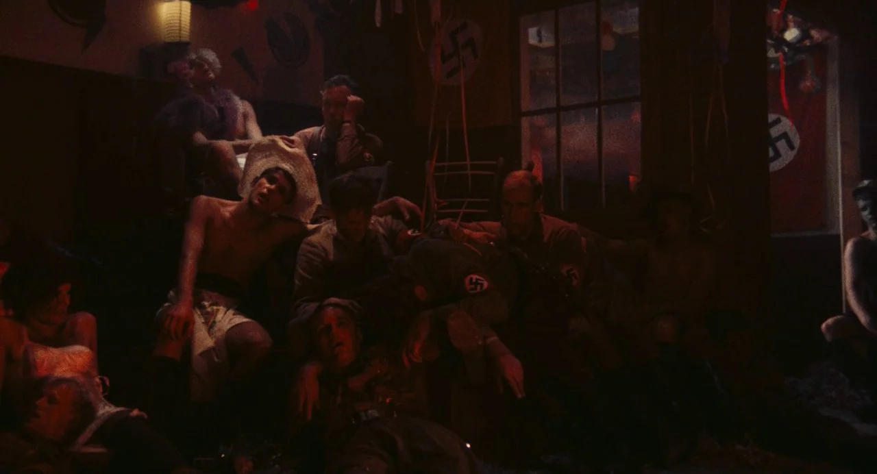 The Damned (1969) movie still: medium — A dim, cluttered nightclub space features red lighting and swastika banners on the walls. A group of…