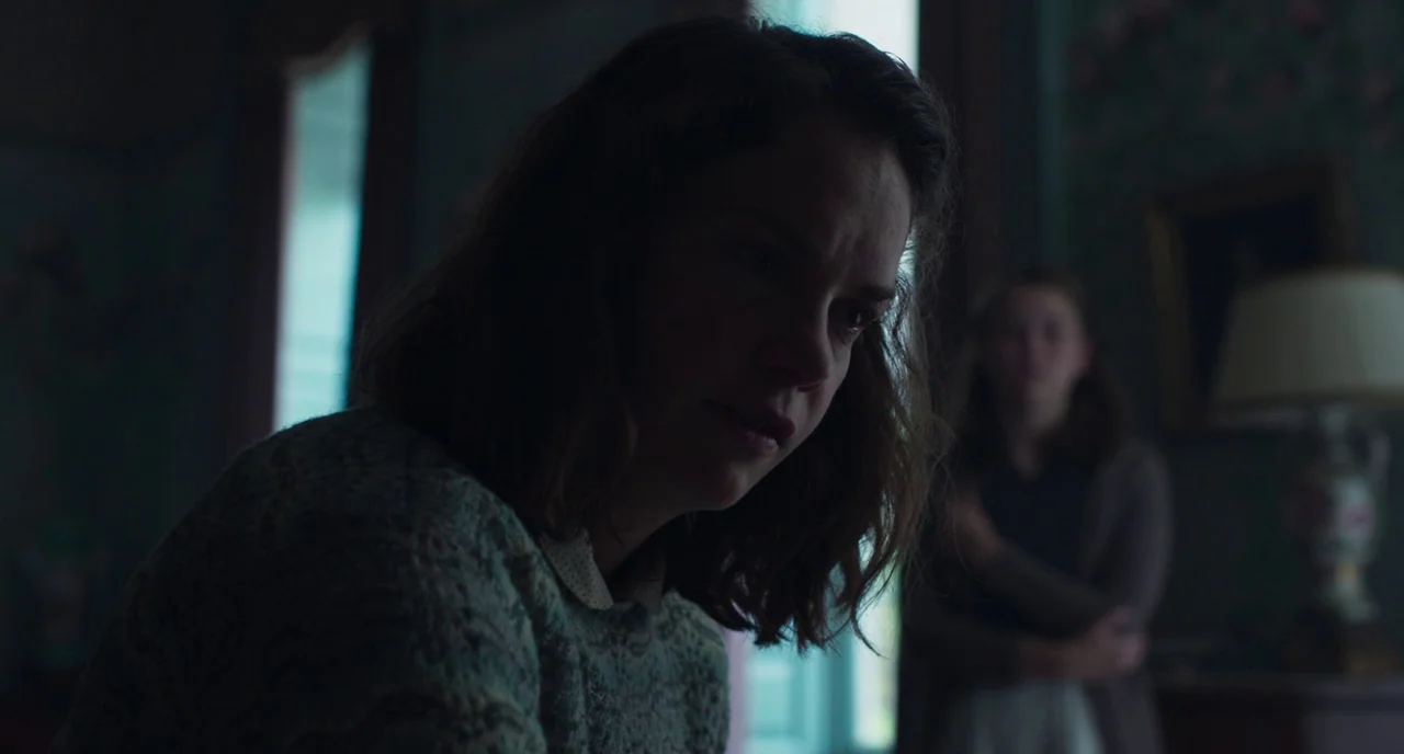 The Little Stranger (2018) movie still: closeup — An interior space features patterned wallpaper and a blurred table lamp in the background. A woman…