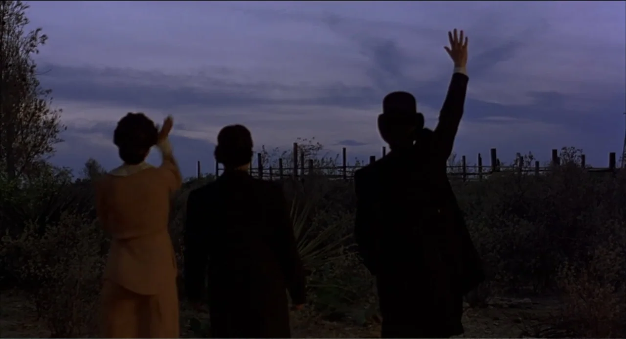Like Water for Chocolate (1992) movie still: fullbody — Three people stand in a sparse, brush-filled field under a fading twilight sky. The trio of…