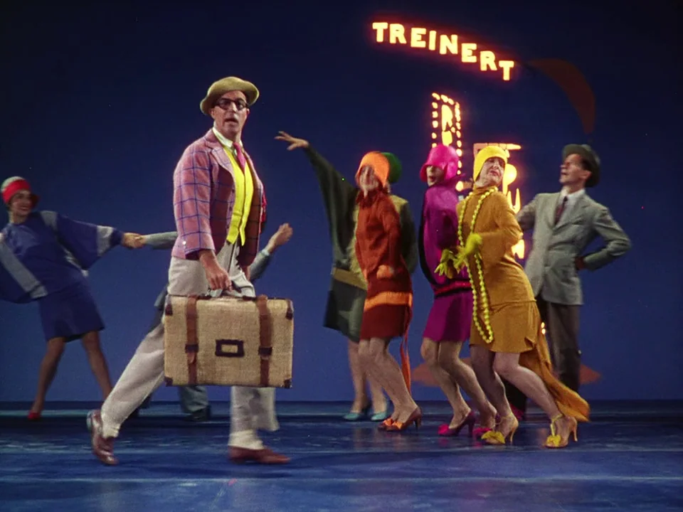 Singin’ in the Rain (1952) movie still: fullbody — A theatrical stage set features a deep blue backdrop with a lit neon sign. Several performers in…