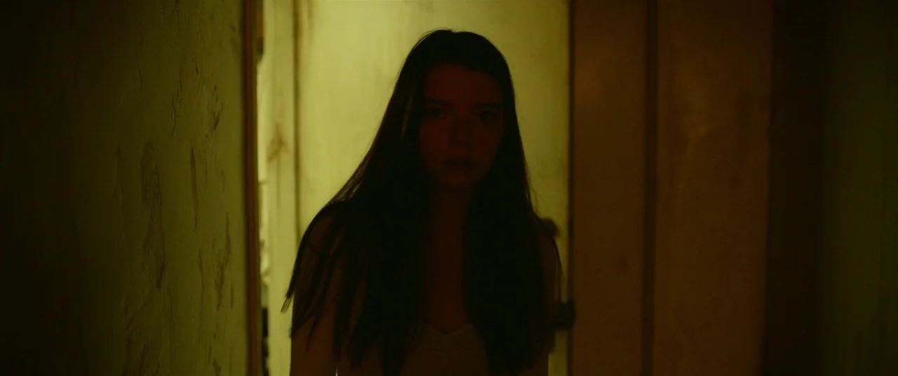 Split (2016) movie still: medium — A dark, narrow corridor with textured walls illuminated by a single warm light source. A woman stands in the…