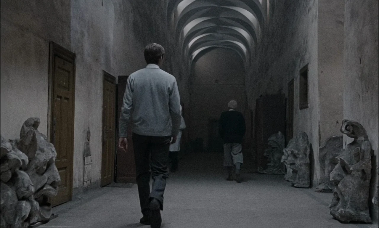 The Third Part of the Night (1971) movie still: fullbody — A long, vaulted stone hallway features weathered plaster walls and stone sculptures on…
