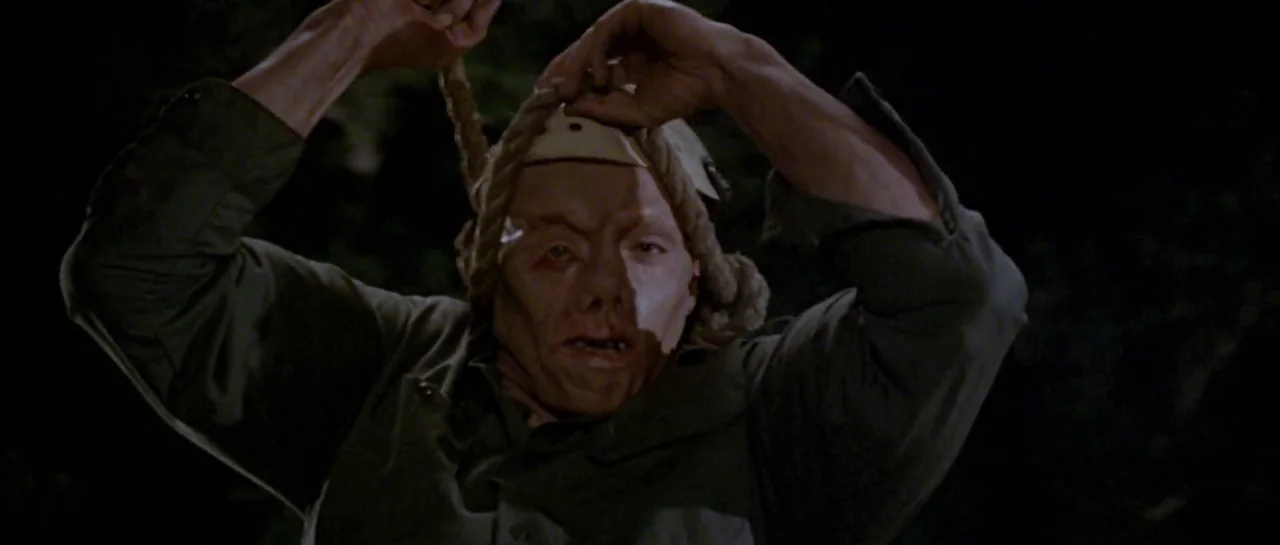 Friday the 13th Part III (1982) movie still: medium — A dark outdoor space with indistinct foliage visible in the deep background. A muscular man…