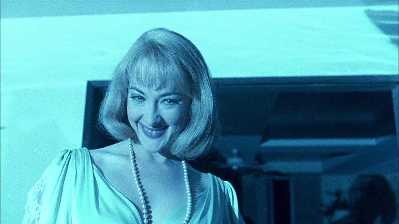 Addams Family Values (1993) movie still: closeup — A woman stands in the dark outdoors, framed against a dimly lit building interior. She looks…