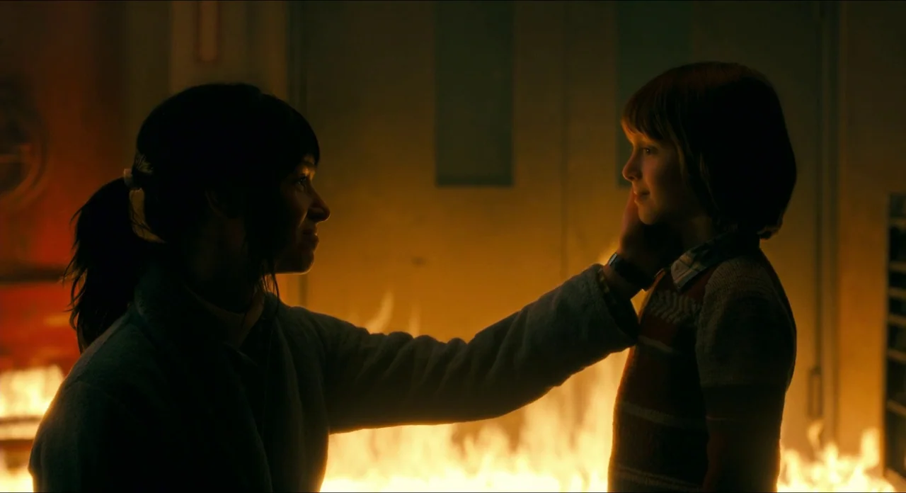 Doctor Sleep movie still: medium — A dark corridor features a wall of bright fire burning along the floor. A woman in a jacket reaches out to touch…