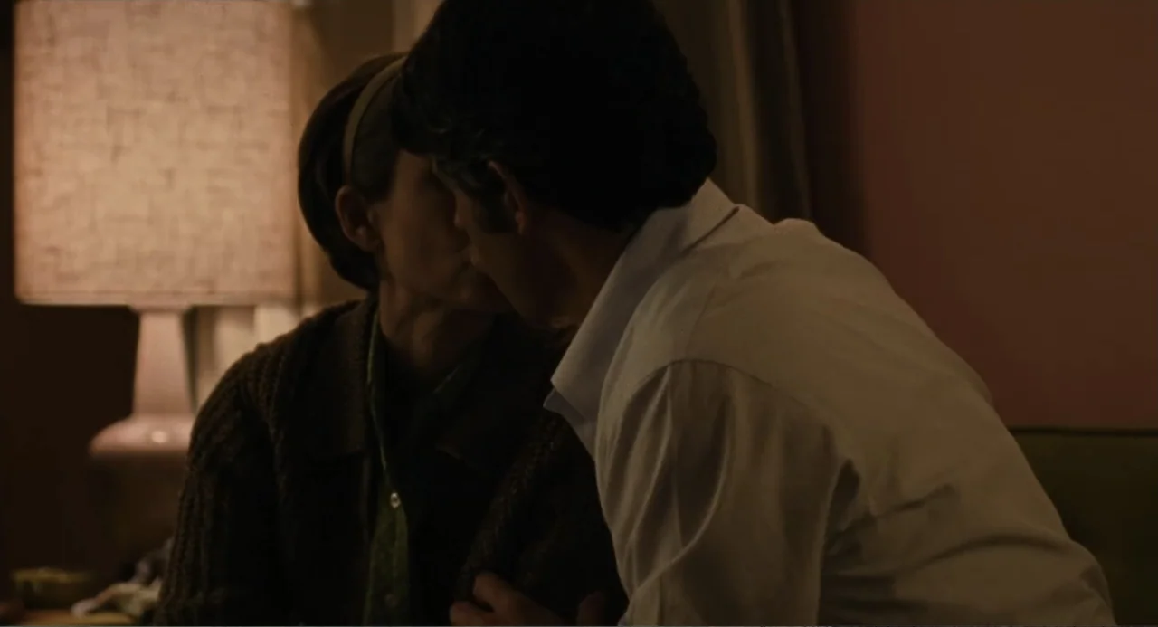 Call Jane (2022) movie still: medium — A dimly lit room interior features a glowing table lamp to the side. A woman and a man kiss each other in the…