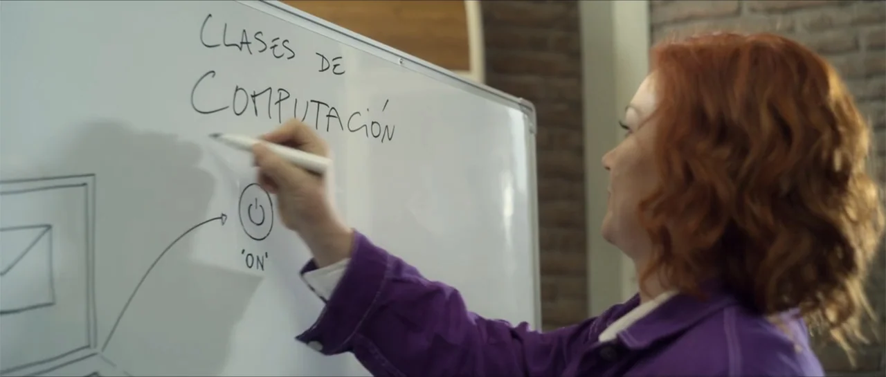 Disconnected 2 (2025) movie still: medium — A classroom interior features a white board mounted against a textured brick wall. A woman with reddish…