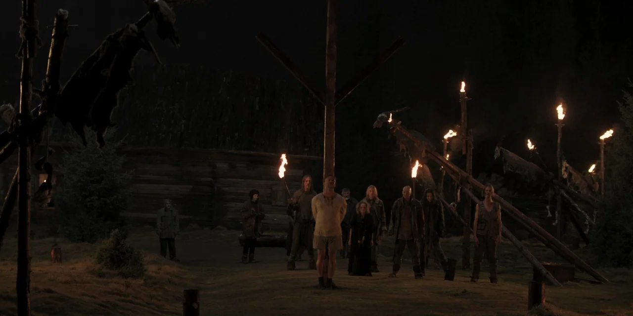 The Ritual (2017) movie still: wide — A night clearing features a central wooden post with a man bound to it. Surrounding individuals hold flaming…