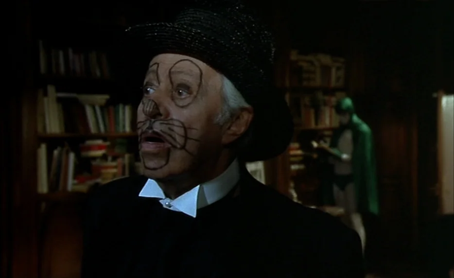 I Want To Go Home (1989) movie still: medium — An older man with drawn-on whiskers stands in a wood-paneled room. Another figure in a green cape is…