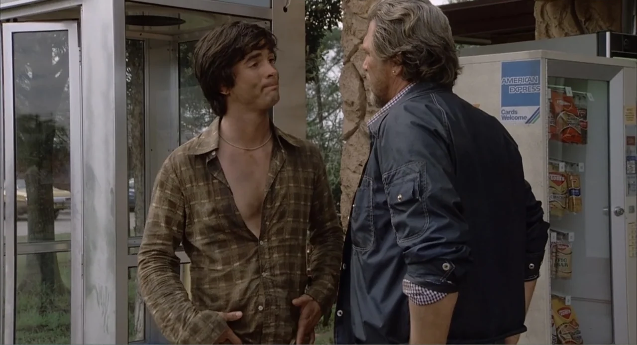 Empire of the Ants (1977) movie still: medium — A parking area near a phone booth and a snack vending machine outdoors. Two men engage in a…