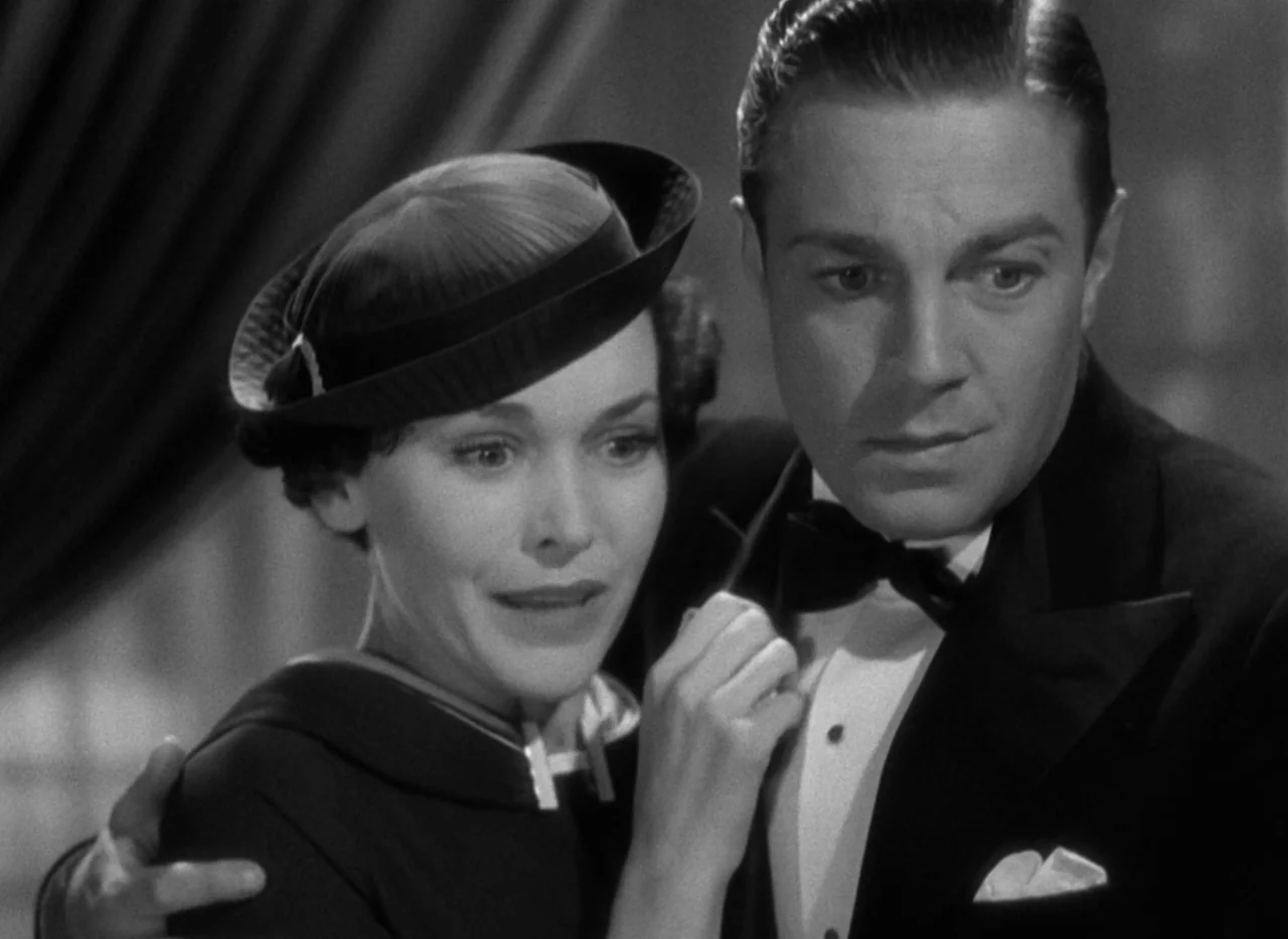 The Thin Man (1934) movie still: medium — A dimly lit interior space with heavy curtains visible in the blurred background. A woman in a dark hat…