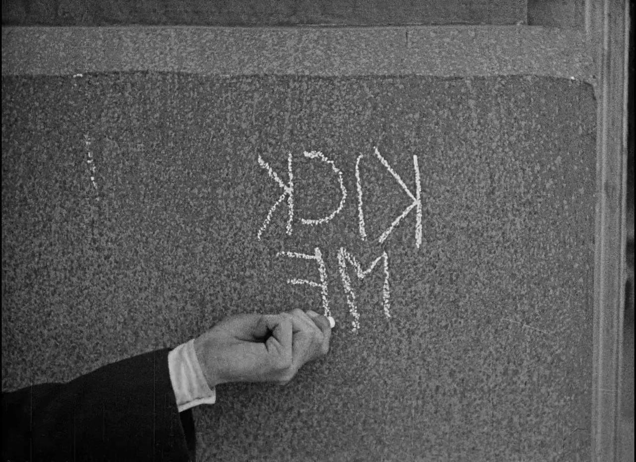 Safety Last! (1923) movie still: closeup — A rough, textured grey stone wall serves as the canvas for handwritten chalk text. A hand writes the…