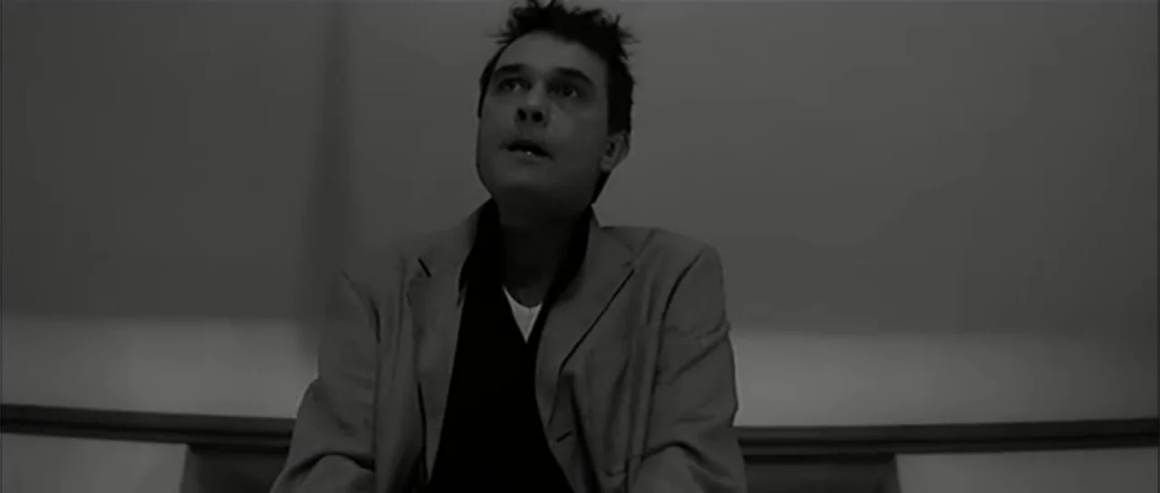 13 Tzameti (2006) movie still: medium — A man sits in a nondescript room with plain walls behind him. The man is looking up toward something above…