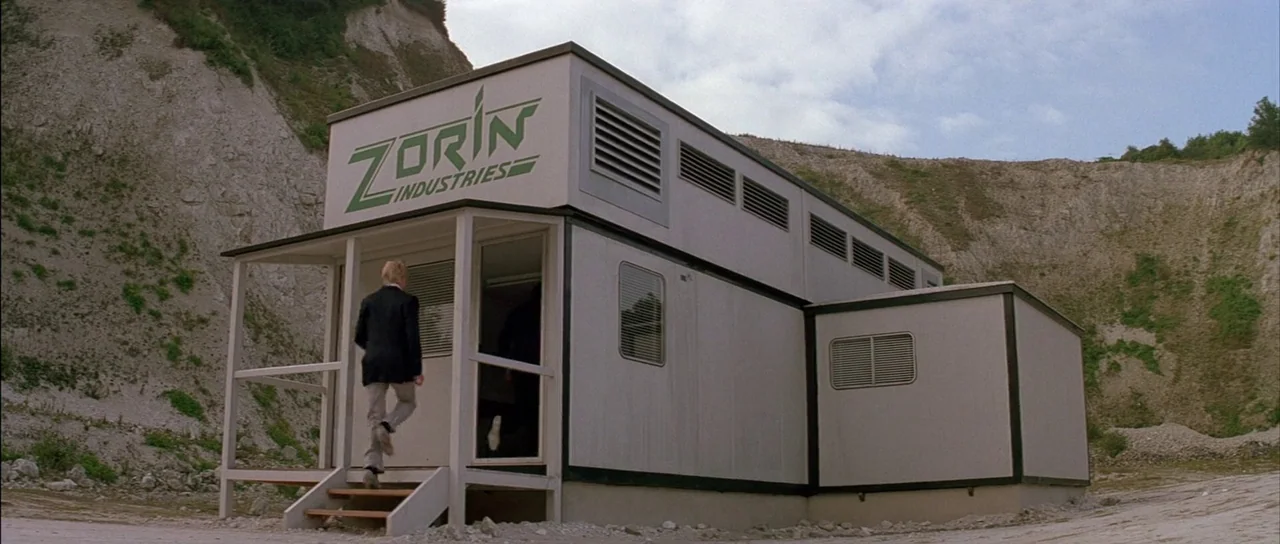 A View to a Kill (1985) movie still: fullbody — A Zorin Industries modular office building sits against a backdrop of steep limestone cliffs. A man…