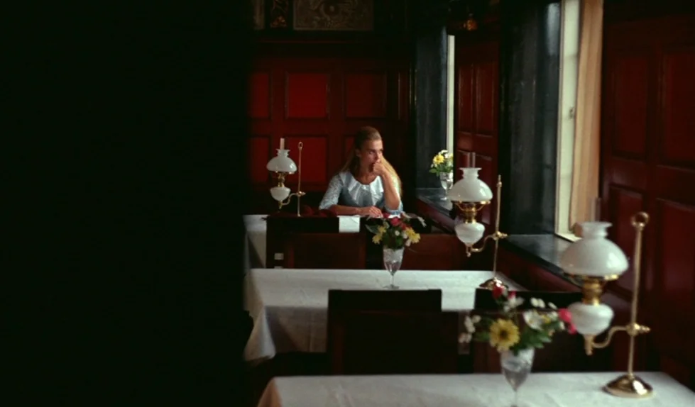 Elvira Madigan (1967) movie still: wide — A dimly lit room with dark red wood paneling and multiple tables set with tablecloths. A young woman with…