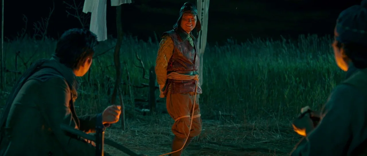 The Good The Bad The Weird (2008) movie still: fullbody — An outdoor encampment at night features tall grass and hanging clotheslines in the dark. A…