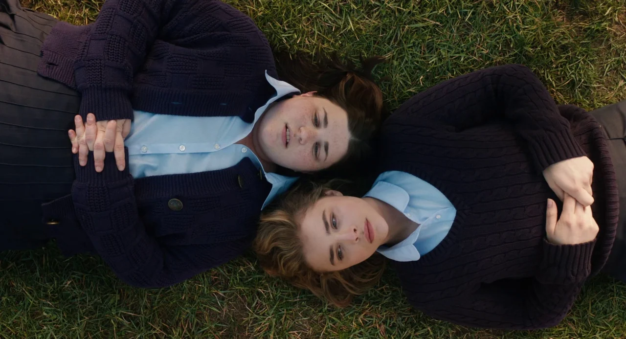 The Miseducation of Cameron Post (2018) movie still: medium — Two teenage girls lie on a patch of green grass in a public area. They are positioned…