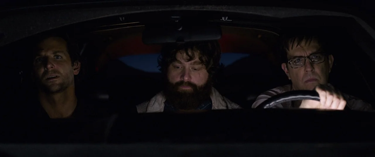The Hangover Part III (2013) movie still: medium — Three men are seated in the front row of a car at night. The interior is dark with soft light…