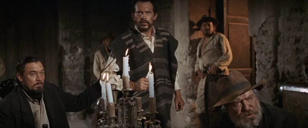 The Wild Bunch (1969) movie still: medium — A dimly lit room with stone walls and wooden architectural details featuring rustic furniture. Four men…