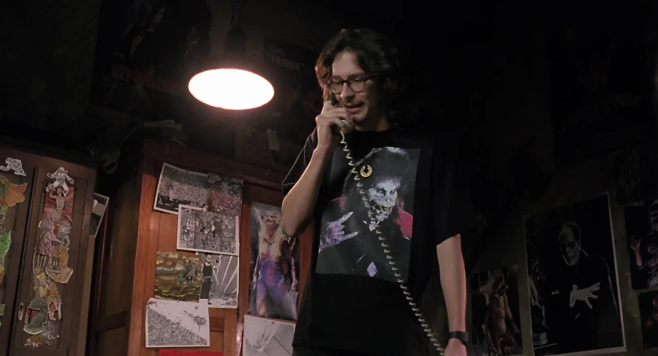 Thesis (1996) movie still: medium — A dark, cluttered room is adorned with various horror movie posters and drawings on walls. A young man stands in…