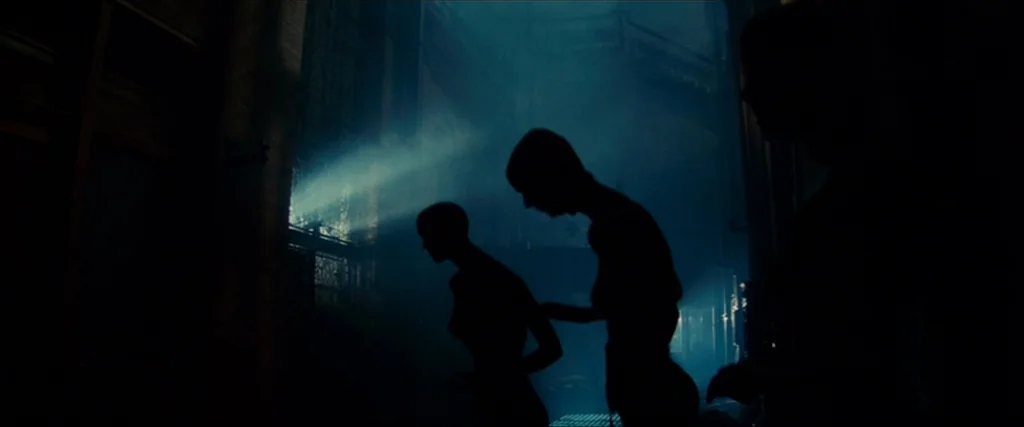 Blade Runner (1982) movie still: medium — A vast, shadowy interior space filled with haze and structural columns. Three silhouettes move slowly…