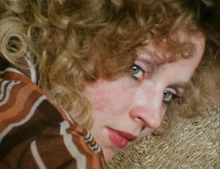 Rio Das Mortes (1971) movie still: closeup — A woman lies on a textured, light-colored surface with a woven pattern. She stares directly towards the…