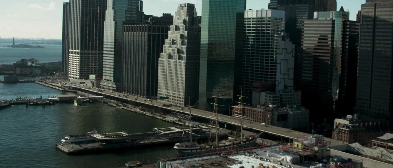 Good Time (2017) movie still: establishing — An aerial view of the Lower Manhattan waterfront features dense skyscrapers and a highway. A historic…