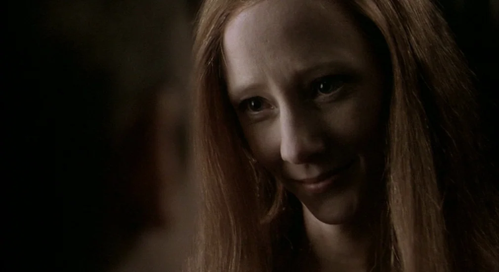 Birth (2004) movie still: closeup — A dark indoor space provides a neutral, dimly lit background. A woman with long hair turns her head to look…